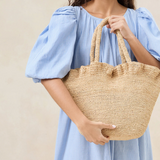 Open tote bag with ruffled detailing in natural crocheted raffia. Features top handle straps and a magnetic closure.